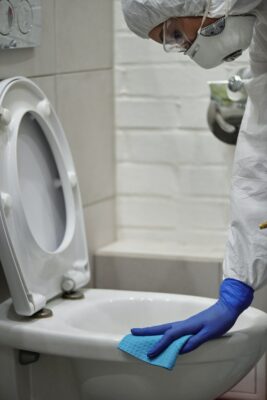 Person in full PPE cleaning toilet in industrial facility for Houston janitorial services